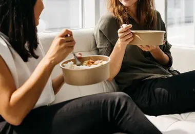 Two women sitting on a couch eating food.