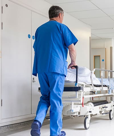 A man in blue scrubs walking down the hallway of a hospital.
