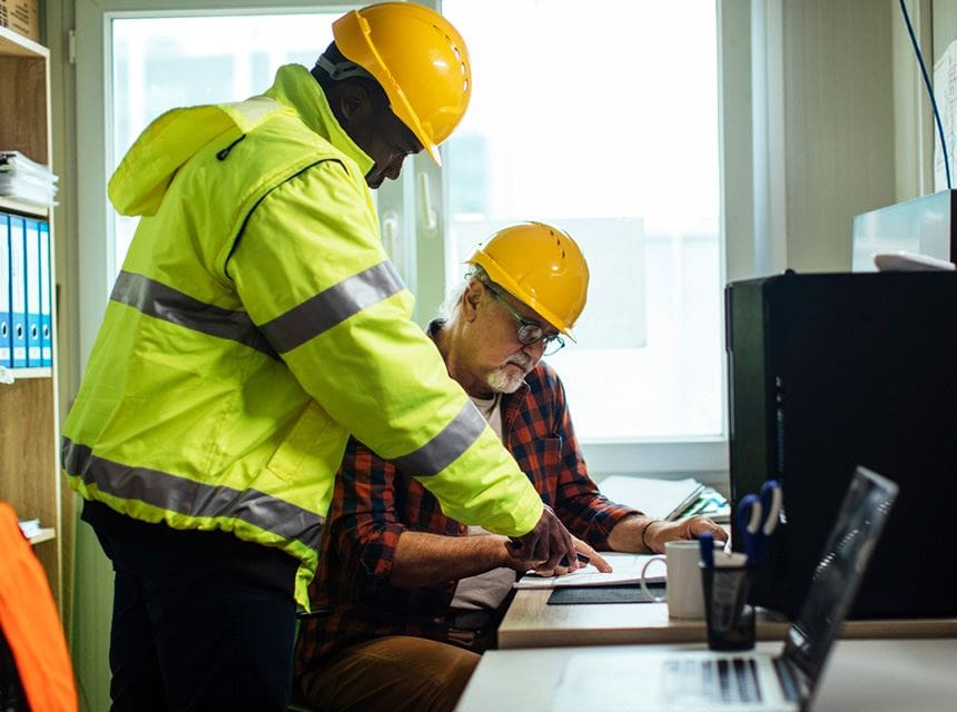 Two men in hard hats working on a computer.