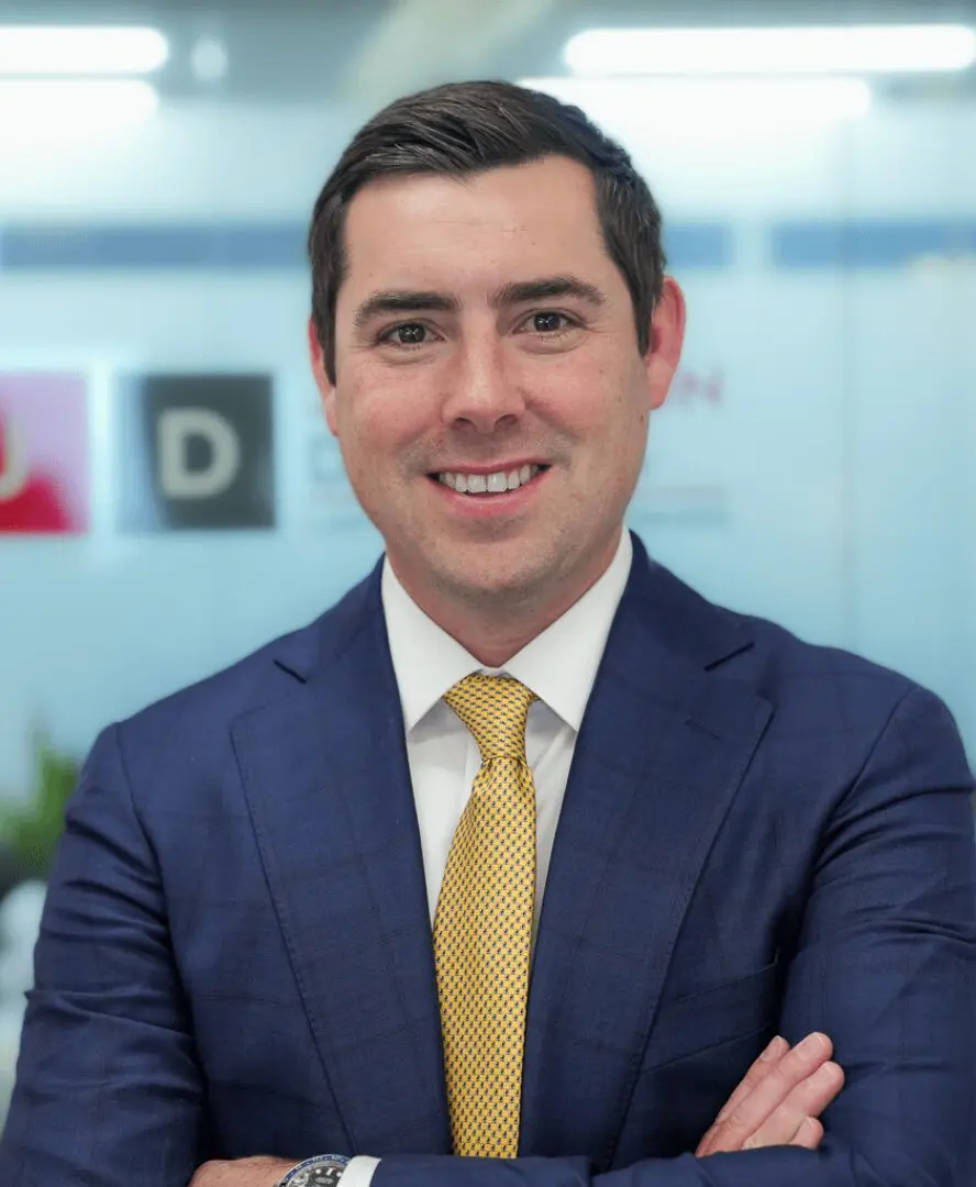 Man in blue suit with yellow tie smiling.